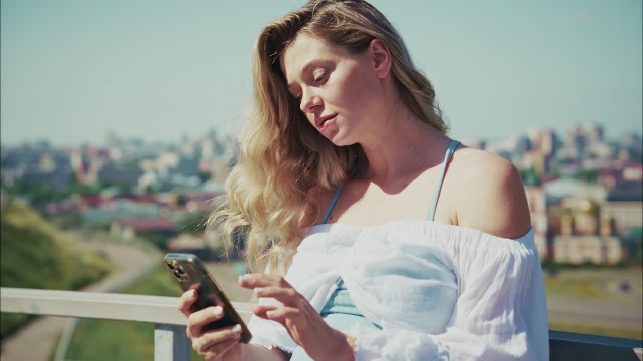 Giovane Donna Bionda Usa lo Smartphone all'Aperto con Vista sulla Città