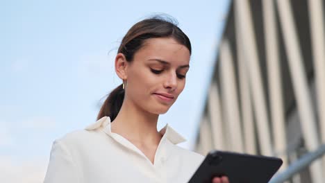 una joven mujer de negocios está de pie en las escaleras y trabaja en un ipad de primer plano