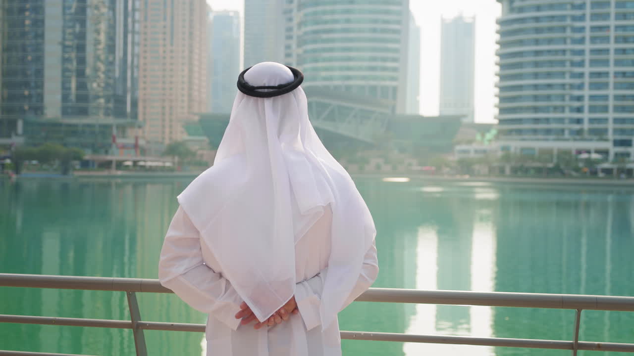 Người đàn ông Emirati mặc trang phục truyền thống màu trắng đứng tại phố đi bộ Dubai Marina và ngắm nhìn
