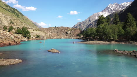 cinematic drone shot flying low over turquoise colored water in the mountains at naltar valley in pakistan, aerial shot