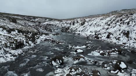 rocky frozen tundra terrain on snowy river in iceland, moody aerial