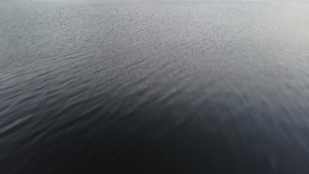 Slow reveal of Mount Shasta volcano from water-level at a nearby lake. The snow-covered mountain peaks out from behind the forested hill, accented by the colors of sunset. 4K California drone shot.