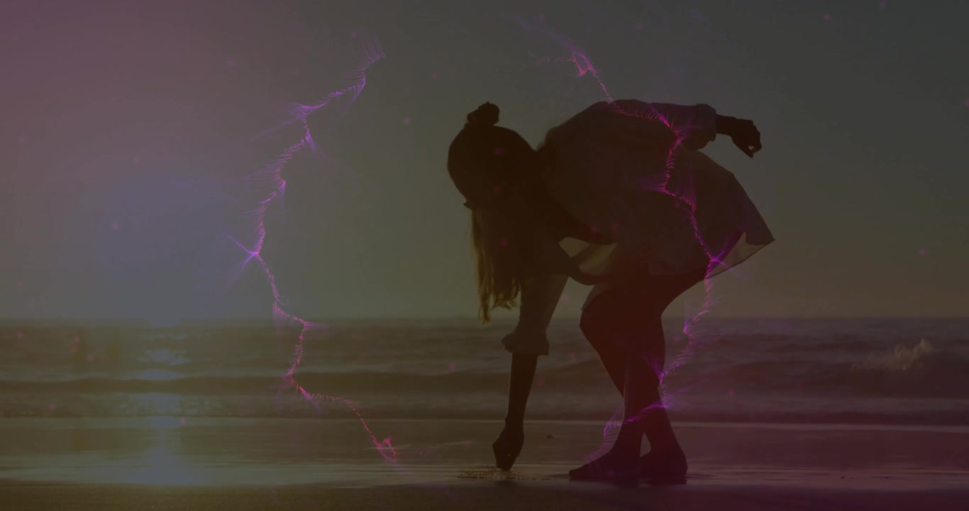 Una donna passeggia sulla spiaggia attivando una tecnologia ad anello viola mentre raccoglie una conchiglia e poi la lancia al cane.