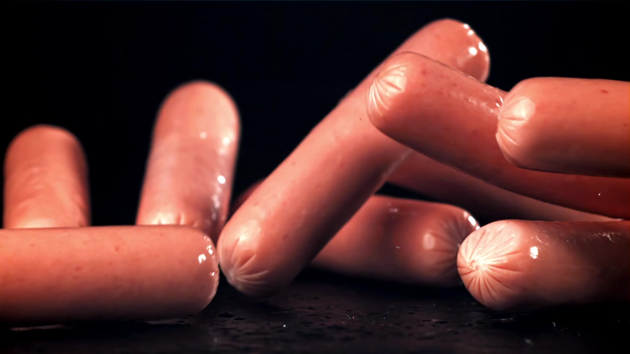 Saucisses crues tombant au ralenti sur une surface noire humide