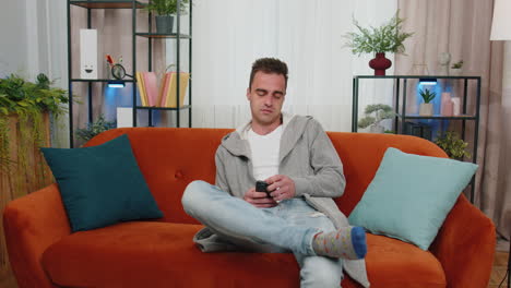 cheerful young man sitting on sofa, using mobile phone share messages on social media application