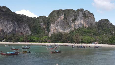 Aerial-Flying-Over-Bay-With-Moored-Traditional-Wooden-Boats-With-View-Of-Limestone-Cliffs-At-Rai-Leh-In-Krabi