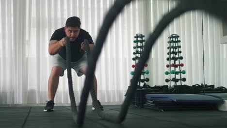 man using battle ropes for whipping exercise in a gym