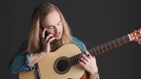 joven caucásico con guitarra teniendo una llamada en el teléfono inteligente.