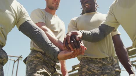 Diverse-group-of-soldiers-making-hand-stack-and-cheering-at-army-obstacle-course-in-the-sun