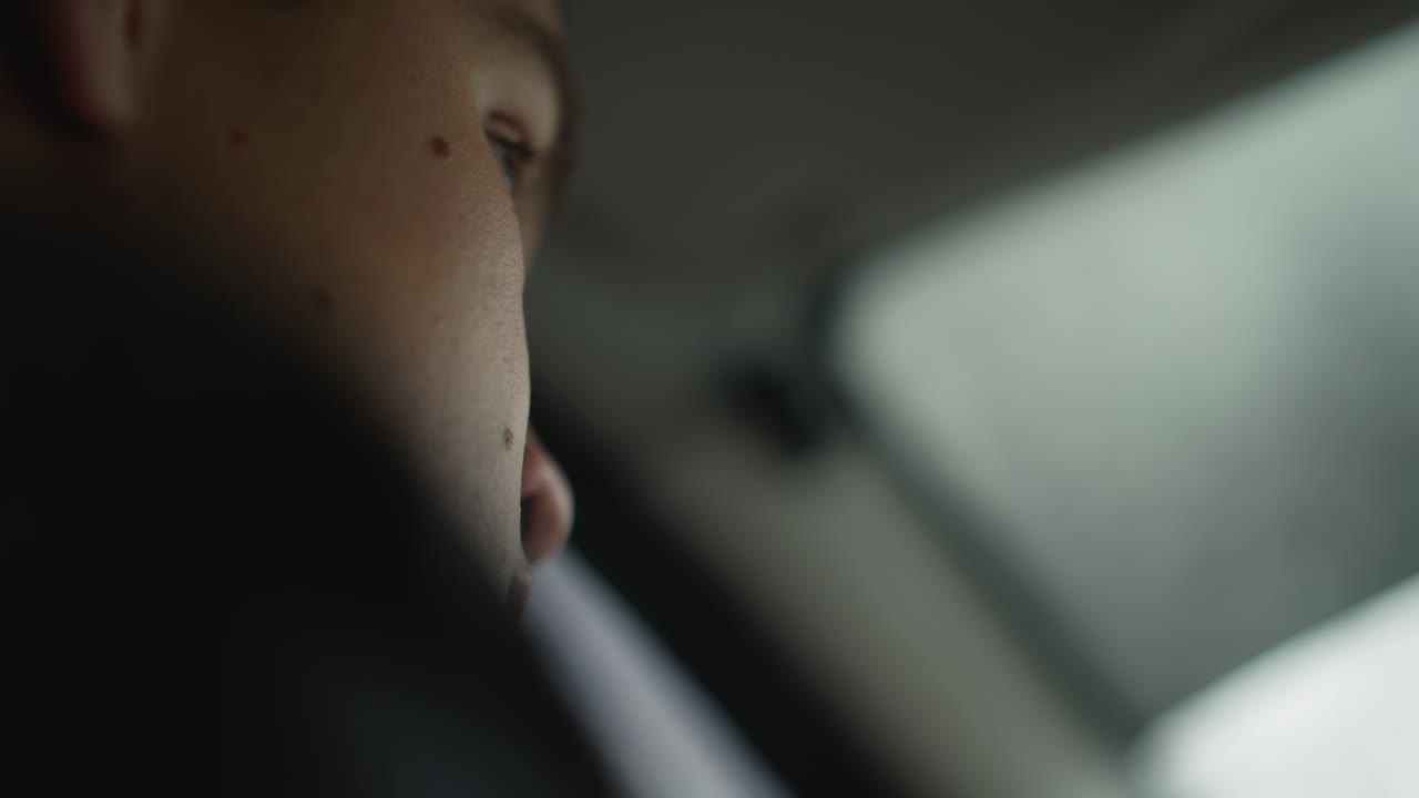 Lower view of young driver focused on road ahead while steering through urban traffic, blurred background outside windshield hints at moving vehicles and city environment in soft natural light