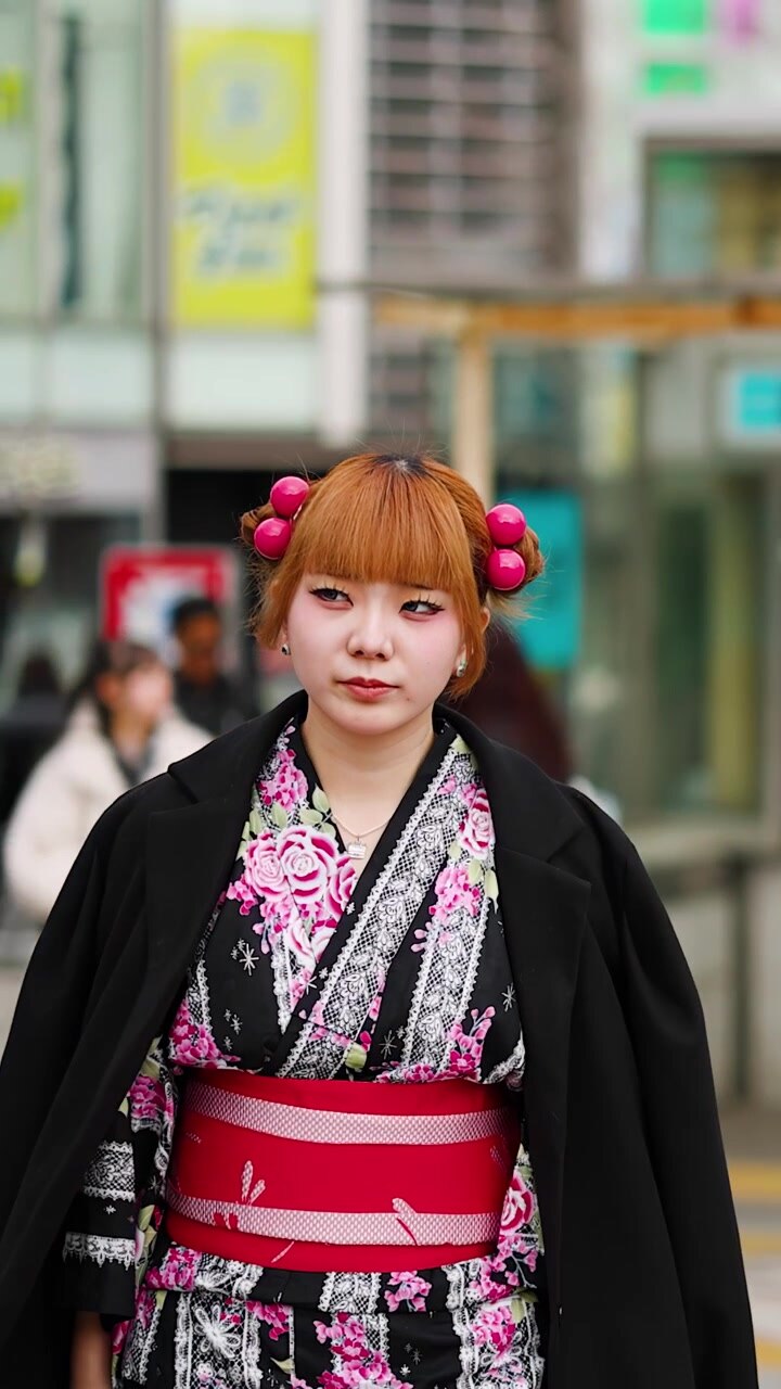 Una giovane donna che indossa un kimono floreale e un cappotto nero cammina attraverso il quartiere Harajuku di Tokyo