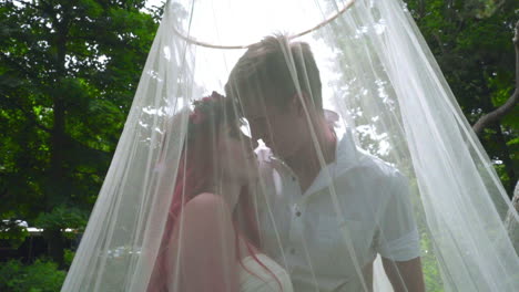 love couple kissing. pregnant couple kissing behind wedding veil at park