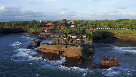 hyperlapse - orbiting tanah lot temple during sunset with tourists standing on the shore - bali, indonesia