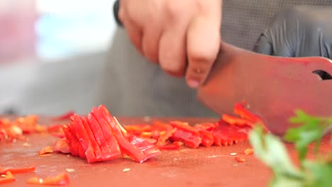 a person chops red bell peppers on a cutting board for food preparation