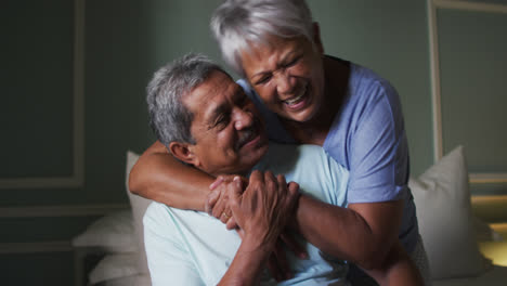 Senior-mixed-race-couple-embracing-and-laughing-in-bedroom