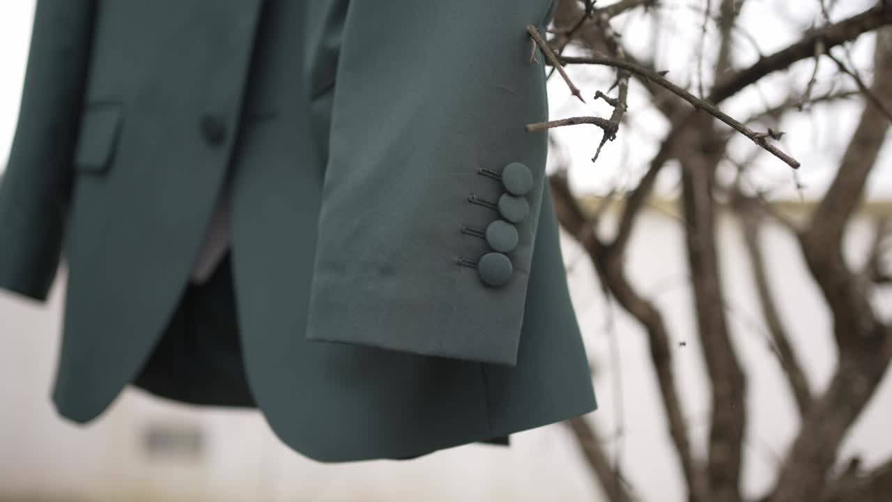 Close up of green suit sleeve with matte buttons hanging from tree branch before ceremony
