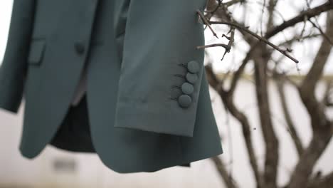 close up of green suit sleeve with matte buttons hanging from tree branch before ceremony