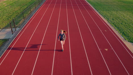 teen girl athlete on a running track warms up towards and under aerial camera