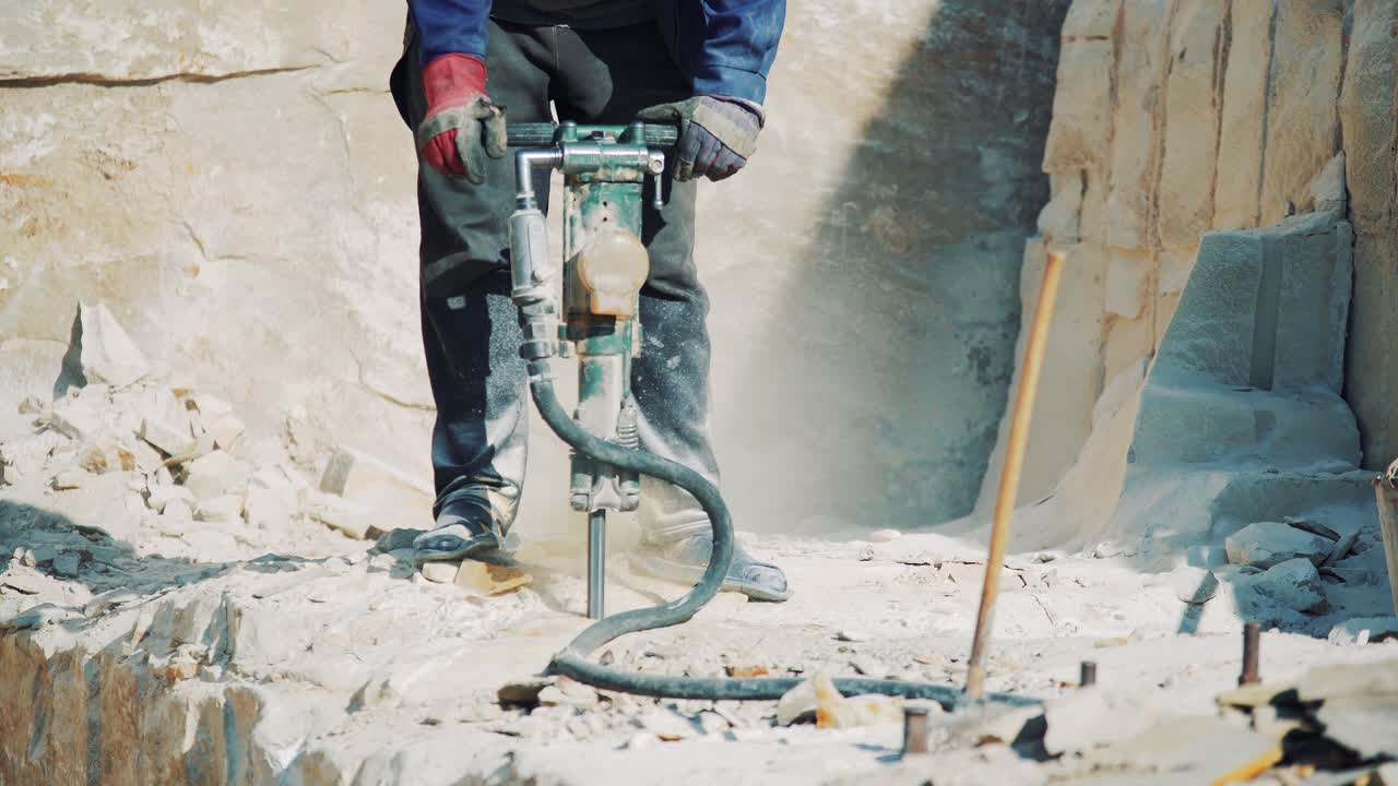 A worker at a stone quarry drills a sandstone block with a jackhammer. Stone mining industry