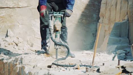 a worker at a stone quarry drills a sandstone block with a jackhammer. stone mining industry