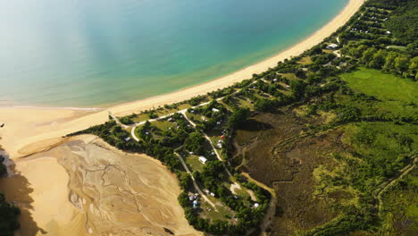 Cozy-campsite-near-golden-beach-of-Pacific-ocean-in-New-Zealand,-aerial-view