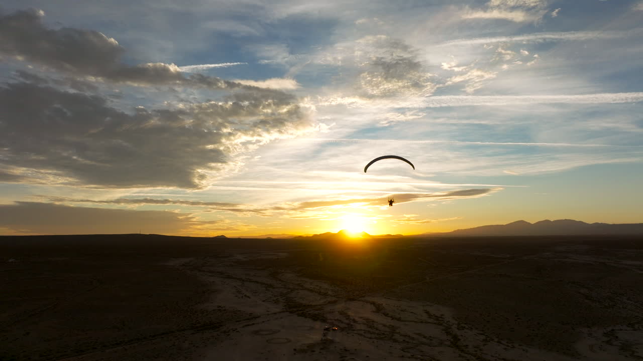 silueta de un parapente motorizado que vuela hacia una puesta de sol dorada sobre el desierto de mojave