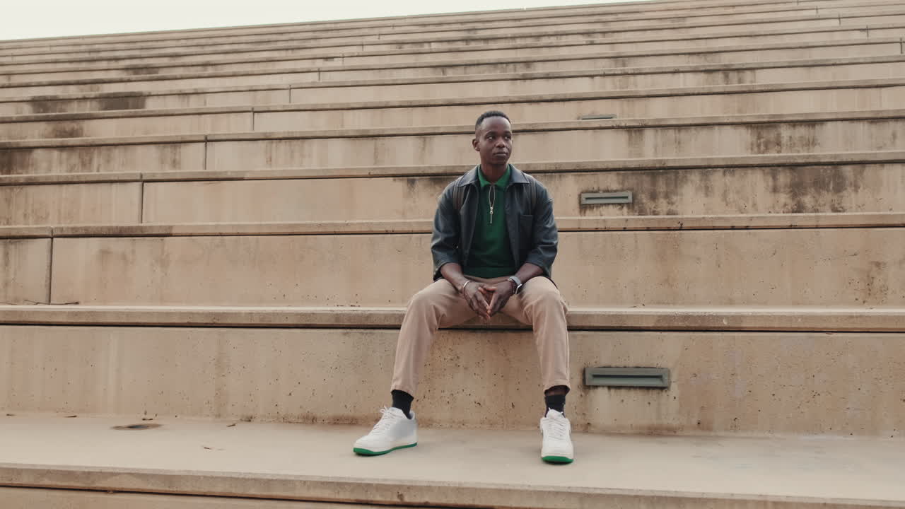 Jeune homme noir assis pensivement sur des marches en béton