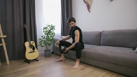 hombre haciendo ejercicios con pesas en casa en la sala de estar en el sofá, mostrando bíceps