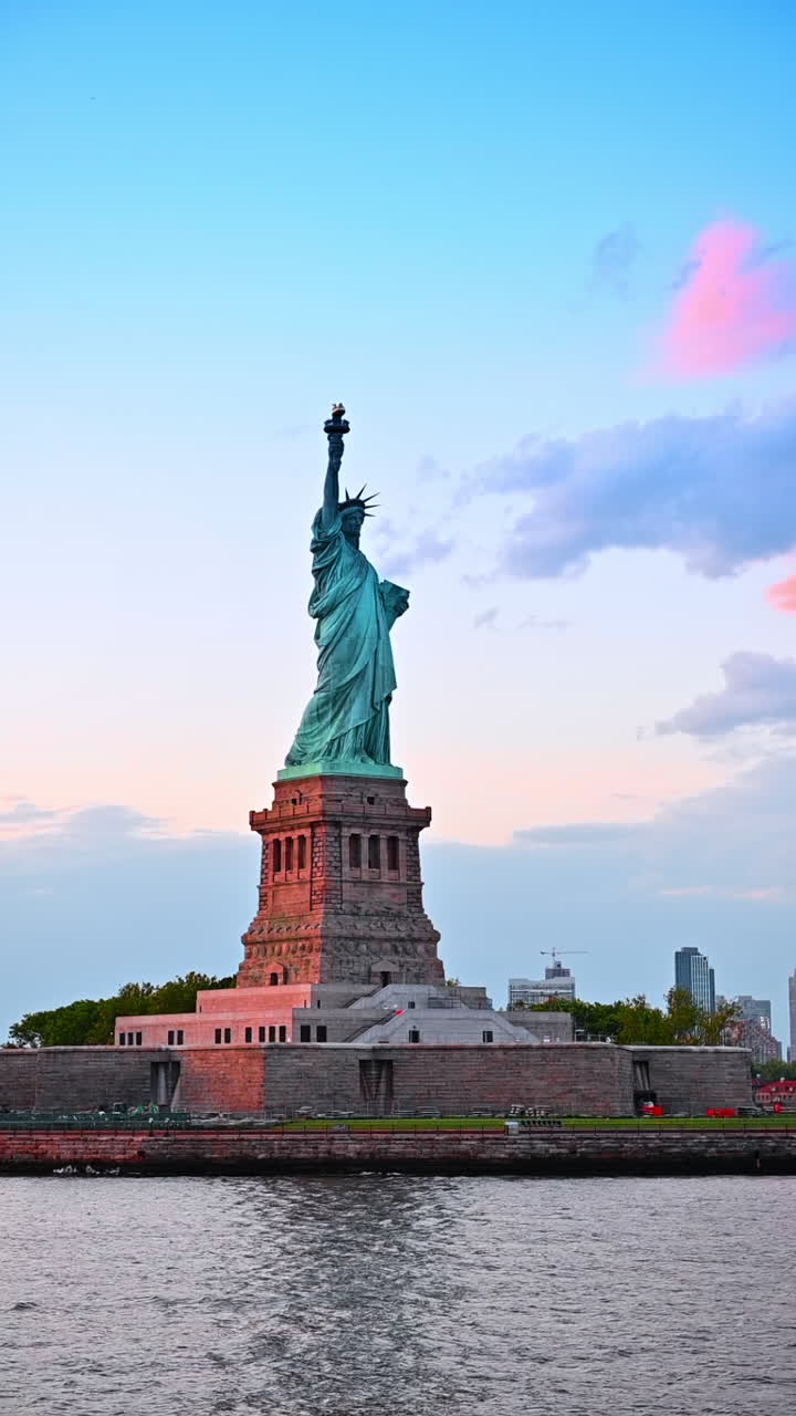 New York, USA, 01 agosto 2025: Un giro nel paesaggio acquatico lungo Liberty Island. Statua della Libertà sotto i raggi del sole al tramonto. Video verticale