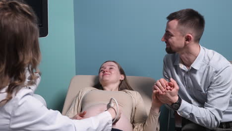 pregnant woman having ultrasound scan at the gynecologist office while loving husband holding her hand 1