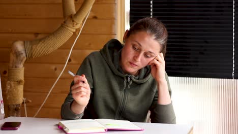 young woman writing in journal notebook sitting at table on porch, tilt up