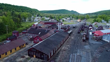 an aerial view of an abandoned narrow gauge coal rail road with rusting hoppers and freight cars and support building starting to be restored