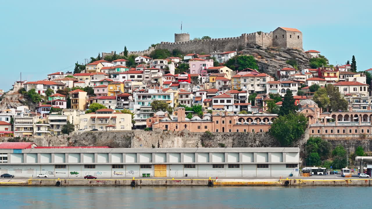 KAVALA, GREECE - SEPTEMBER 23, 2020: View of the town from the water. Rows of residential buildings, ancient fortress on the hill, Aegean sea rocky coast