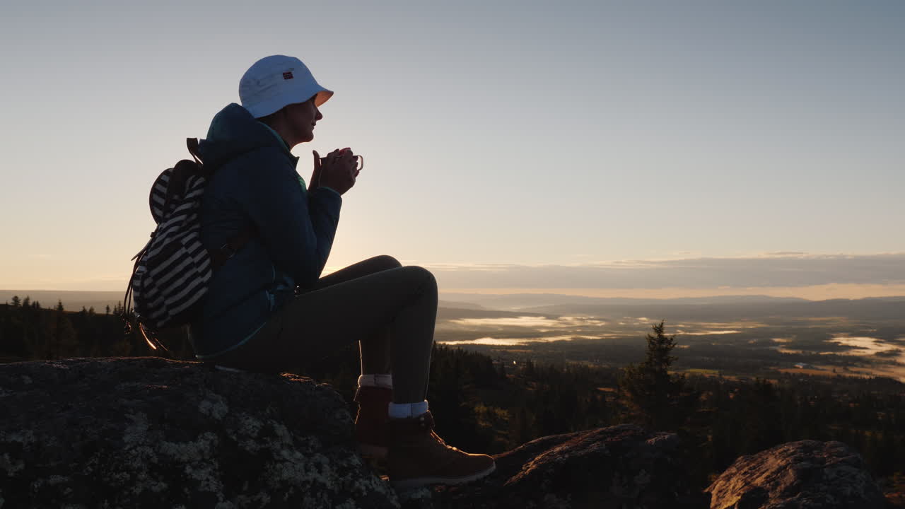 한 여행자가 산 정상에 있는 머그잔에서 차를 마신다.
