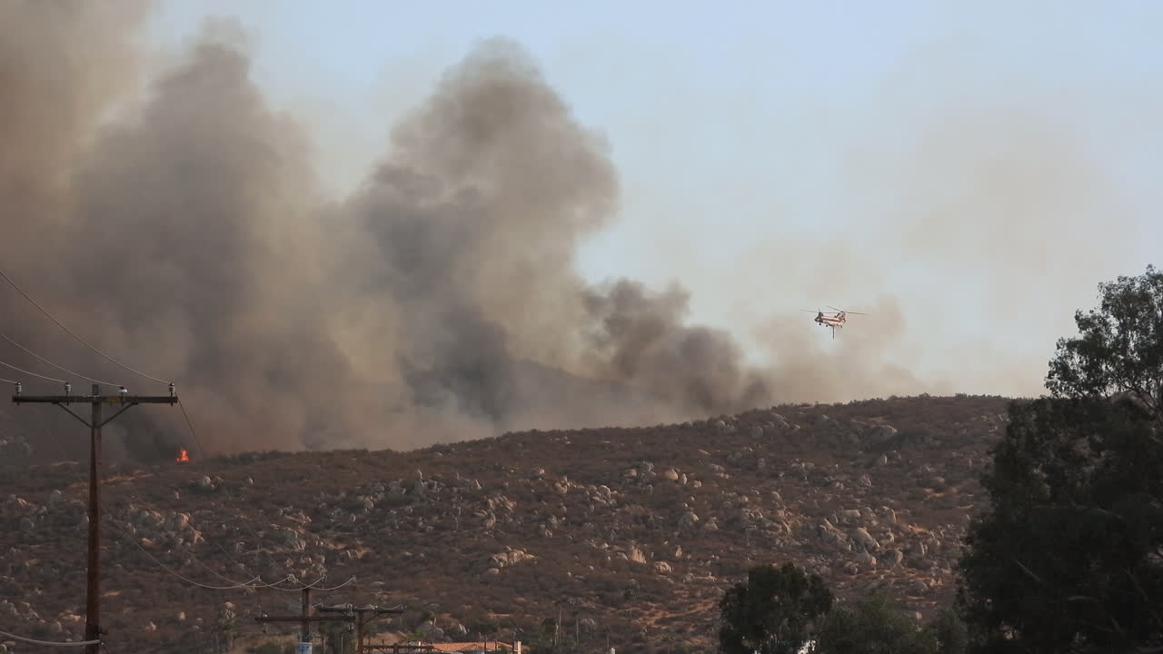 Elicottero che sgancia un'enorme quantità d'acqua sull'incendio di Fairview, con nuvole di fumo che bloccano la vista