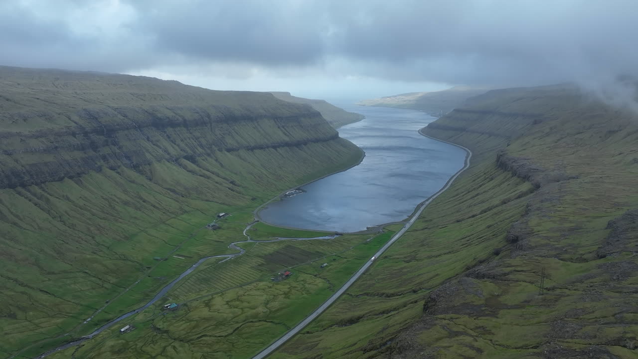 Majestic aerial flight over a long fjord nestled between towering green mountains in the Faroe Islands