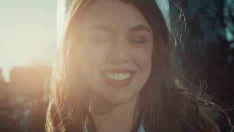 close-up lens flare portrait, happy beautiful 20s caucasian woman with wind in hair smiles at camera outside slow motion