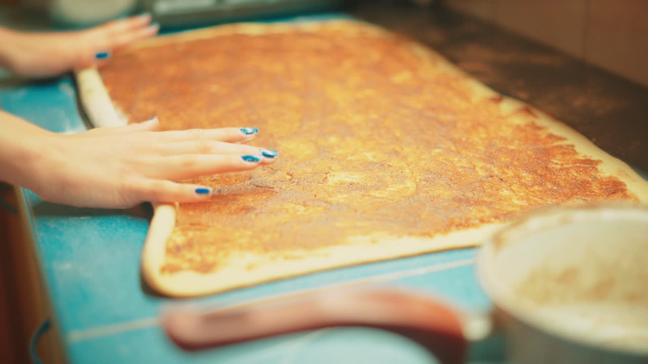 Primo piano di mani di adolescente che arrotolano con cura l'impasto preparato con ripieno di cannella fino a ottenere una forma di rotolo compatto. Fase finale di modellatura per le tradizionali girelle alla cannella fatte in casa