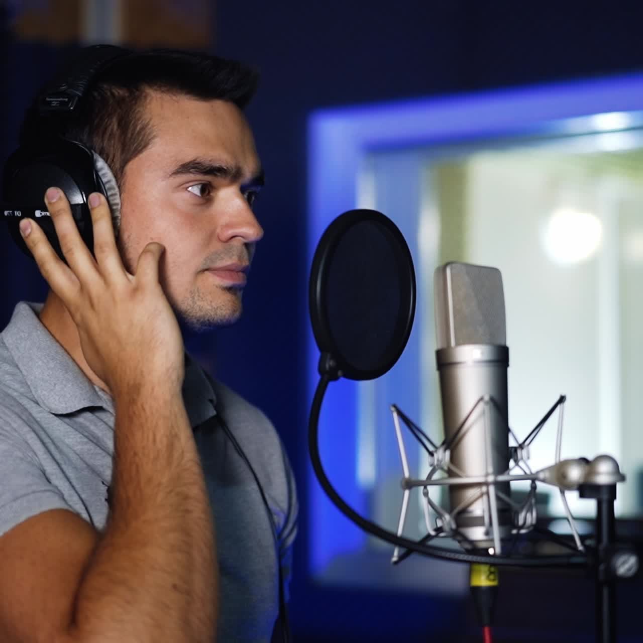Male handsome singer standing in front of professional microphone. Man has headphones on his head and listens to music in them