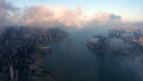 Revealing Victoria harbour and Hong Kong urban skyline behind low hanging clouds during sunrise. drone dolley shot