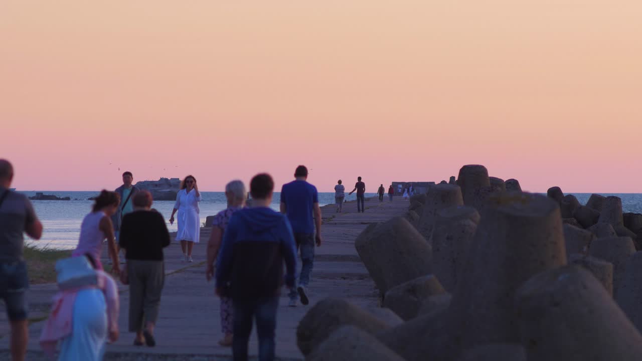 People walking on the Karosta Northern Pier at romantic red glowing sunset, medium shot from a distance