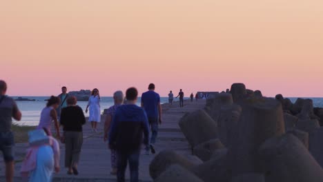 people walking on the karosta northern pier at romantic red glowing sunset, medium shot from a distance
