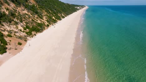 Langsame-Drohnenschwenks-Zeigen-Die-Wunderschönen-Strände-Rund-Um-Fraser-Island,-Umgeben-Von-Aquafarbenem-Wasser-Und-Farbenfrohen-Sanddünen-An-Einem-Sonnigen-Tag