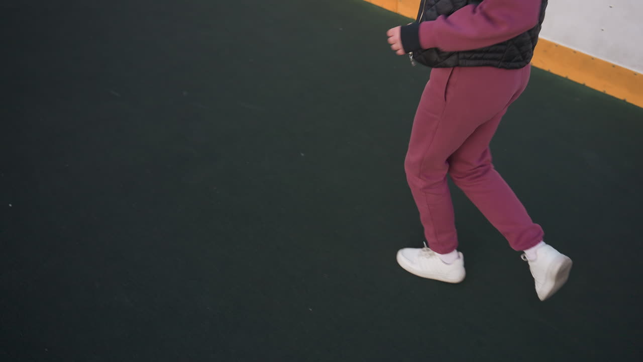 High angle view of legs of fitness enthusiast jogging around curved barbed wire sports court under pastel dusk sky, white sneakers stepping on asphalt adjacent to yellow edged barrier panels