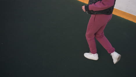 high angle view of legs of fitness enthusiast jogging around curved barbed wire sports court under pastel dusk sky, white sneakers stepping on asphalt adjacent to yellow edged barrier panels