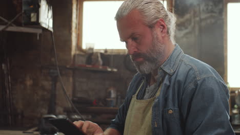 bearded man using digital tablet at work in smithy