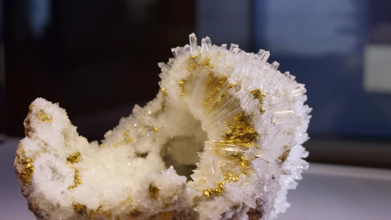 Tight close-up motion shot of white quartz geode showing dense radial cluster of needle-like prismatic crystals and scattered gold-colored metallic inclusions lining interior cavity