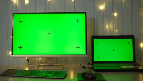 green screen laptop and pc monitor on a homework desk in dark room with garland background