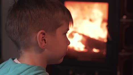 little boy sit by burning fireplace watch fire, and enjoy a hot tee cozy atmosphere