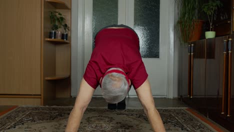 anciano caucásico de edad avanzada en ropa deportiva en la sala de estar, haciendo ejercicios de flexión matutinos en casa